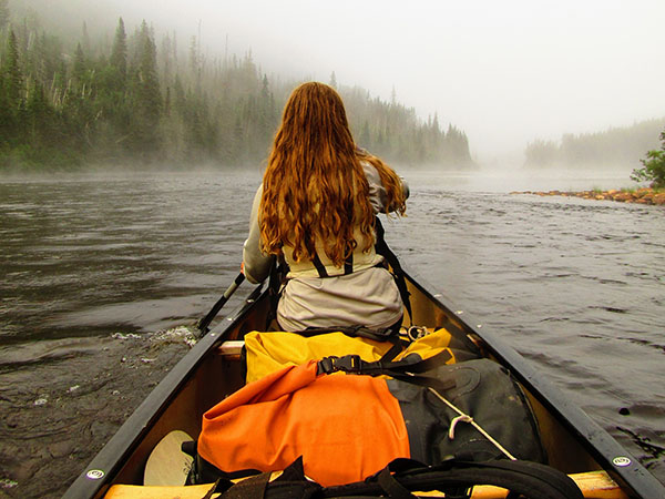 Camper at front of canoe paddling in misty river