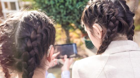 2 girls — one with hearing aid — looking at smartphone
